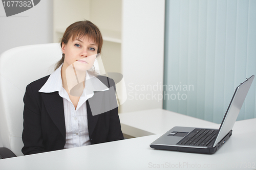 Image of Serious woman sits at table at light office with laptop