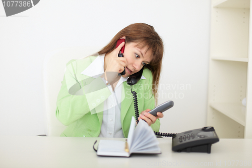 Image of Beautiful woman - secretary speaks by several phones simultaneou