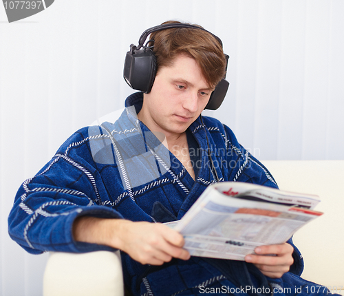 Image of Man in big ear-phones on sofa reads newspaper