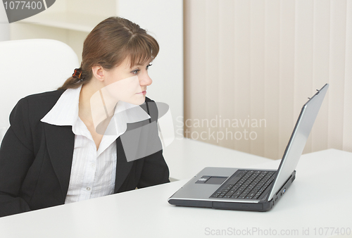 Image of Young woman sits at table at light office with laptop