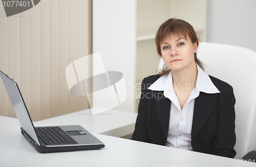 Image of Serious woman sits at table at light office with laptop