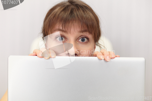 Image of Amusing girl hides behind laptop screen