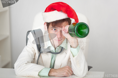 Image of Amusing guy in Christmas cap with bottle in a hand