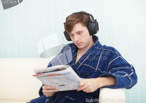 Image of Person in big ear-phones on sofa reads newspaper