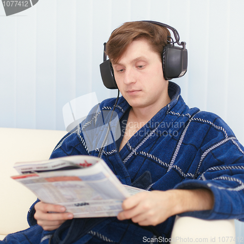 Image of Man in big ear-phones on sofa reads newspaper