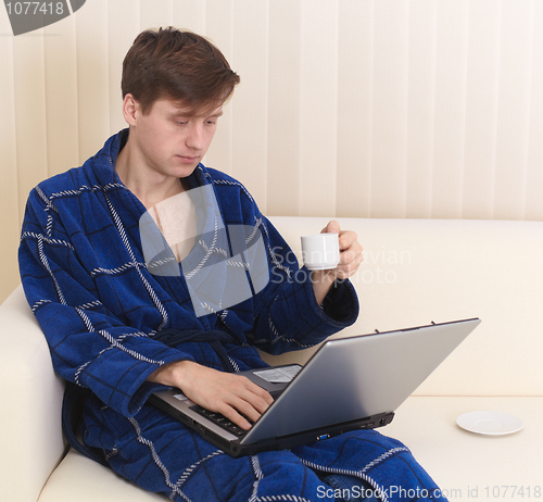 Image of Guy works in Internet on sofa and drinks coffee