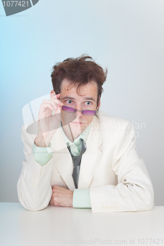 Image of Tousled young man in eyeglasses sitting at a table