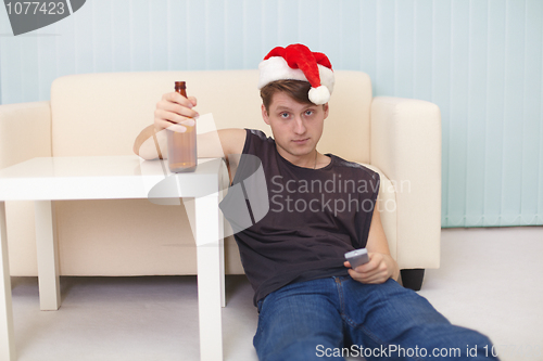 Image of Young man in christmas hat sits on a floor with beer