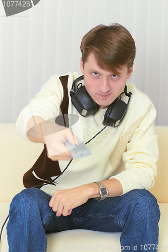 Image of Person with remote control and ear-phones watches TV on sofa