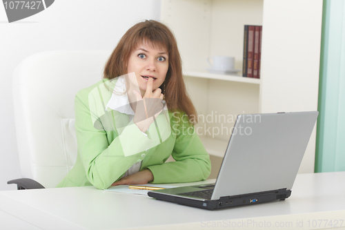 Image of Funny woman sits at table at office with laptop