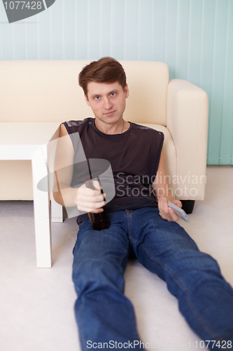 Image of Young man sits on floor with beer at TV