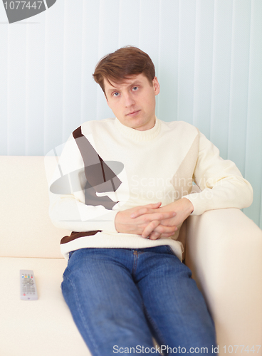 Image of Young man sits on sofa with remote control