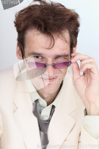 Image of Artful businessman looks over eyeglasses crookedly grinning