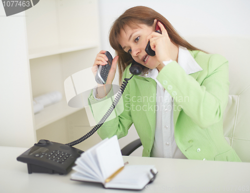 Image of Young woman - secretary speaks by several phones simultaneously