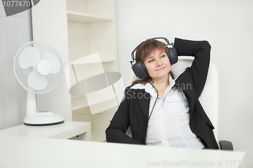 Image of Young beautiful woman at office with ear-phones and listens to m