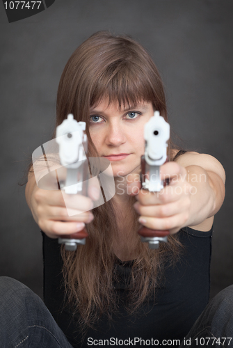 Image of Young serious woman aims from two pistols