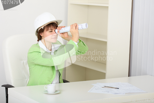 Image of Young woman in helmet sits at table with draft in hands