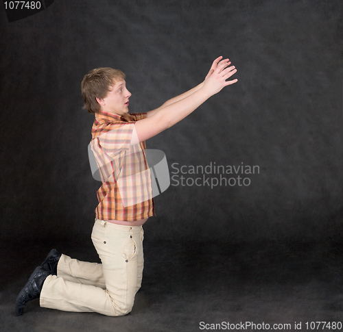 Image of Amusing young man is kneeling and stretch hands to something