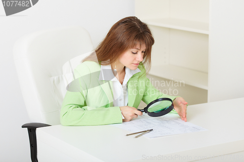 Image of Young girl sits at table with big magnifier in hands