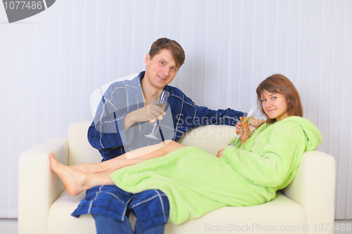 Image of Young couple drinks sparkling wine on sofa in dressing gowns