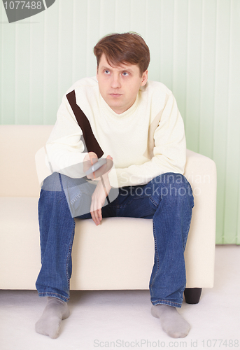 Image of Young man sits on sofa with remote control