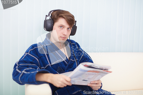 Image of Man in big ear-phones on sofa reads newspaper