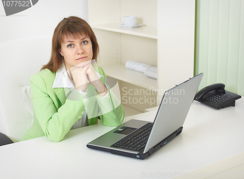 Image of Young woman with laptop sits at table at light office
