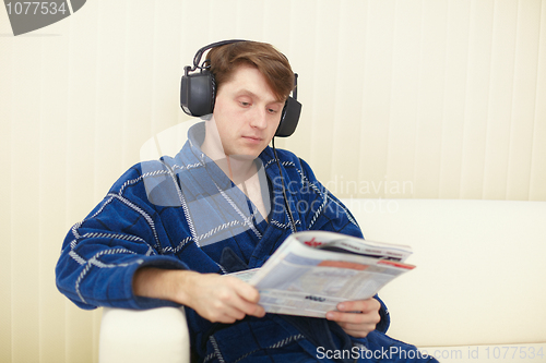 Image of Man in big ear-phones on sofa reads journal