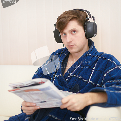 Image of Person in big ear-phones on sofa reads newspaper