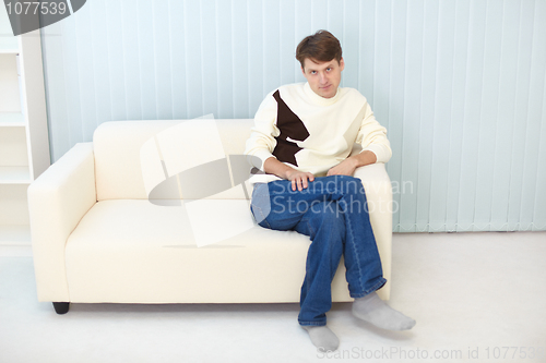 Image of Person in jeans and sweater sits on sofa