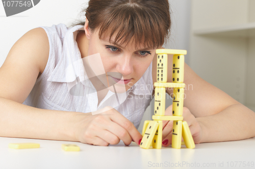 Image of Young woman accurately builds tower of dominoes