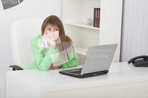 Image of Young woman thoughtfully sits on workplace at office