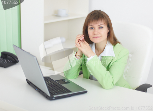 Image of Young woman with laptop sits at table at light office