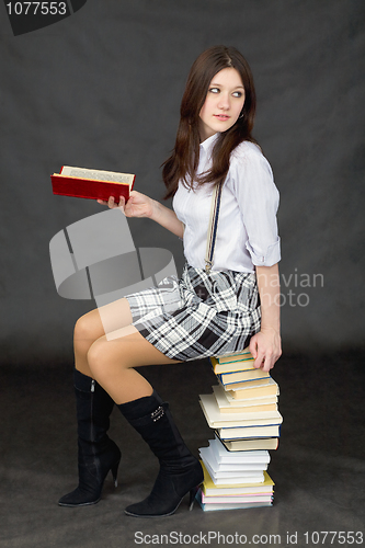 Image of Schoolgirl sits on big pile of books against dark background