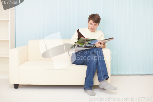 Image of Young man sits on sofa with journal