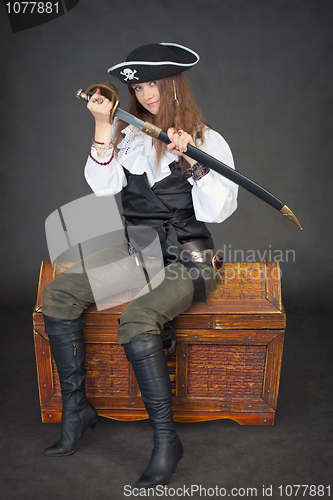 Image of Woman pirate gets sabre from a sheath sitting on chest with trea