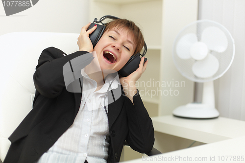 Image of Young woman with ear-phones on head sings on a workplace