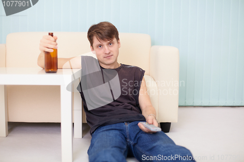 Image of Man sits on floor with beer bottle in a hand