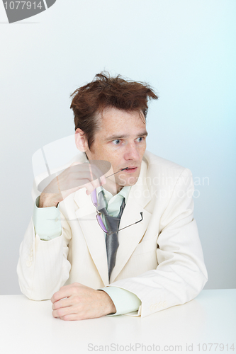 Image of Confused tousled man sits at table