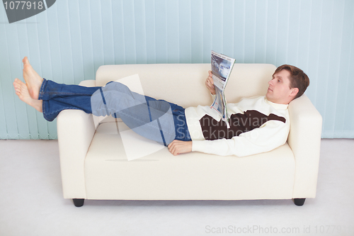 Image of Young man reads magazine lying on couch