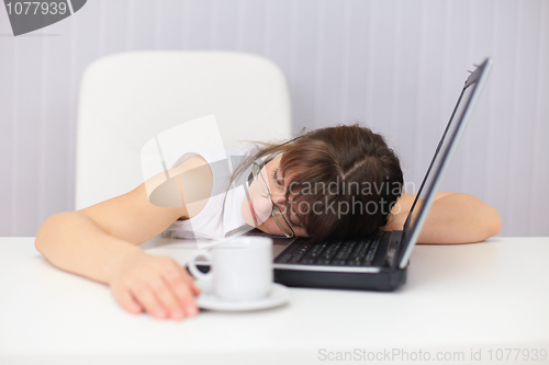Image of Young woman comically sleeps on laptop at office