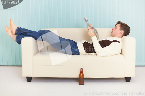 Image of Person reads magazine comfortably lying on sofa