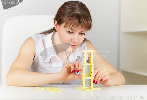 Image of Young woman builds tower on a table of dominoes