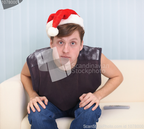 Image of Young man sits on sofa in a red Christmas cap
