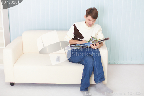 Image of Man sits on sofa with newspaper and remote control