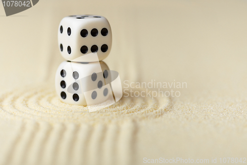 Image of Two white dice with black dots on sand