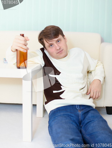 Image of Drunken man sits on floor with beer bottle