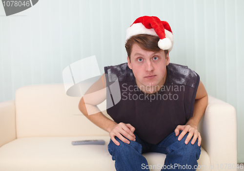 Image of Person in Christmas cap sits on sofa and watches TV