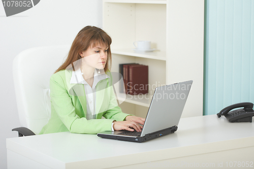Image of Young woman sits at table at light office with laptop
