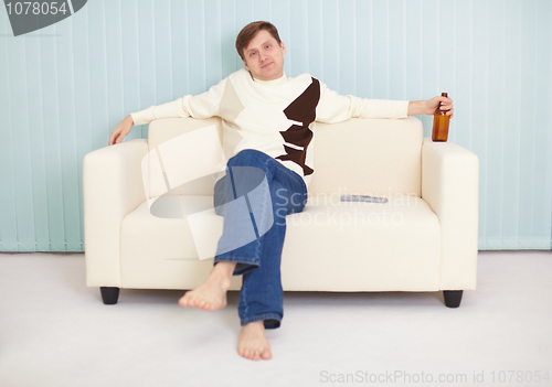 Image of Young guy has rest on a sofa with beer and TV